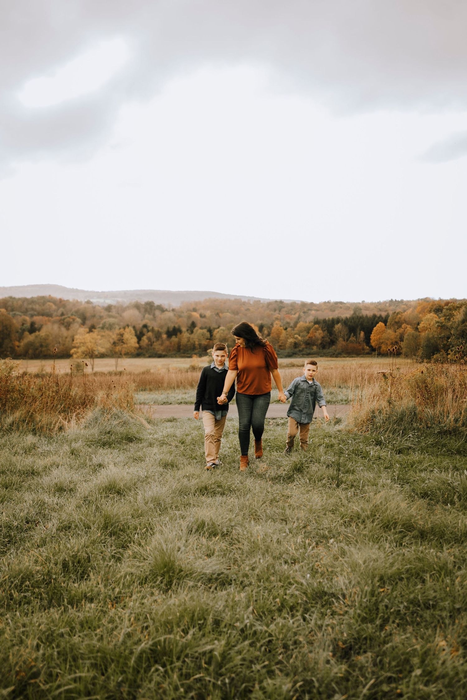 Family walking together through golden autumn field with mountains in background.
