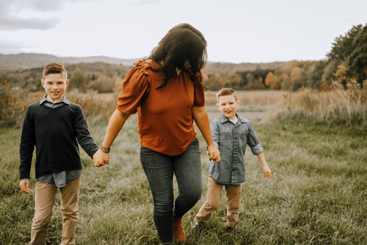 Family enjoying a walk together on grassy hillside during fall season.