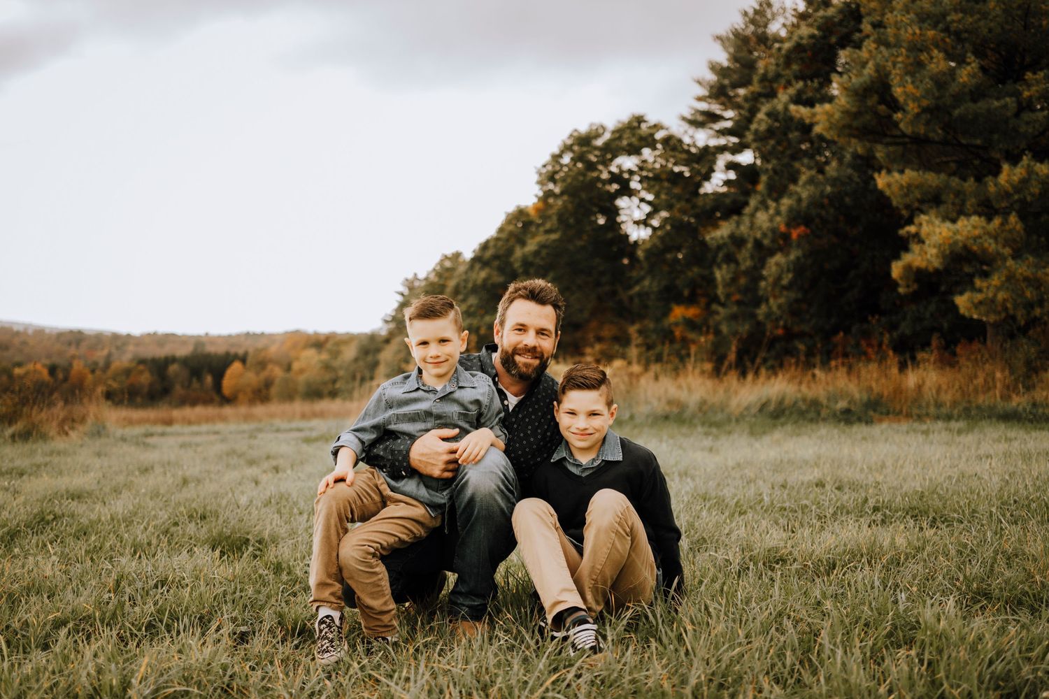 Casual outdoor family portrait with everyone sitting close together on grassy hill.