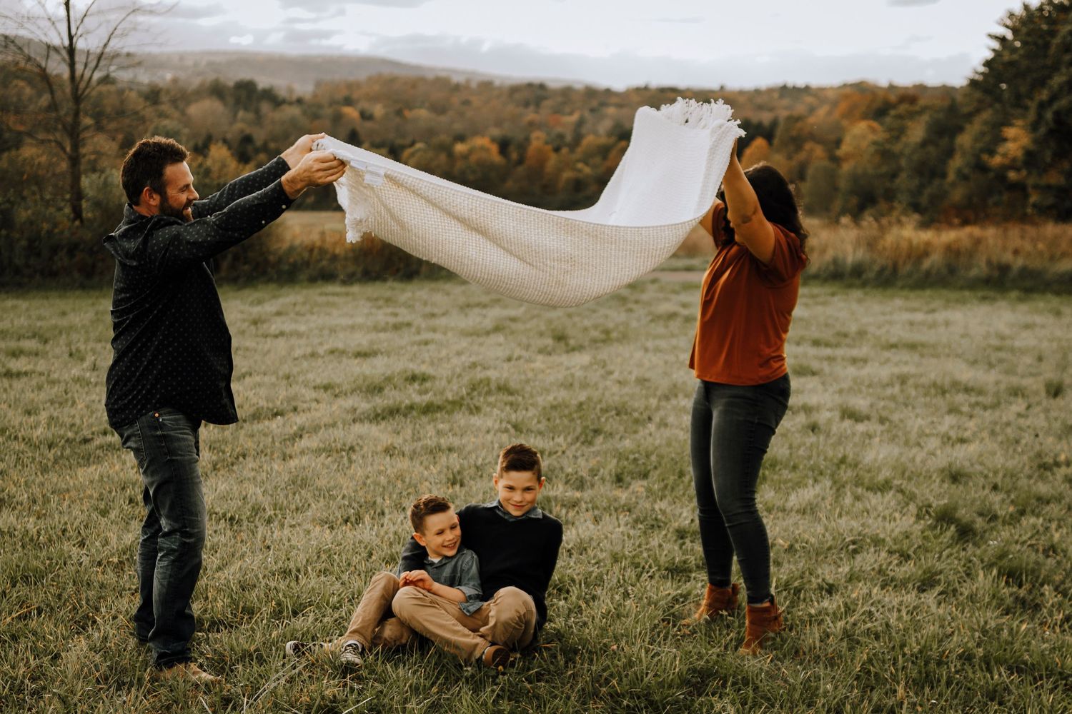Family playing with white fabric in field during autumn photo session.
