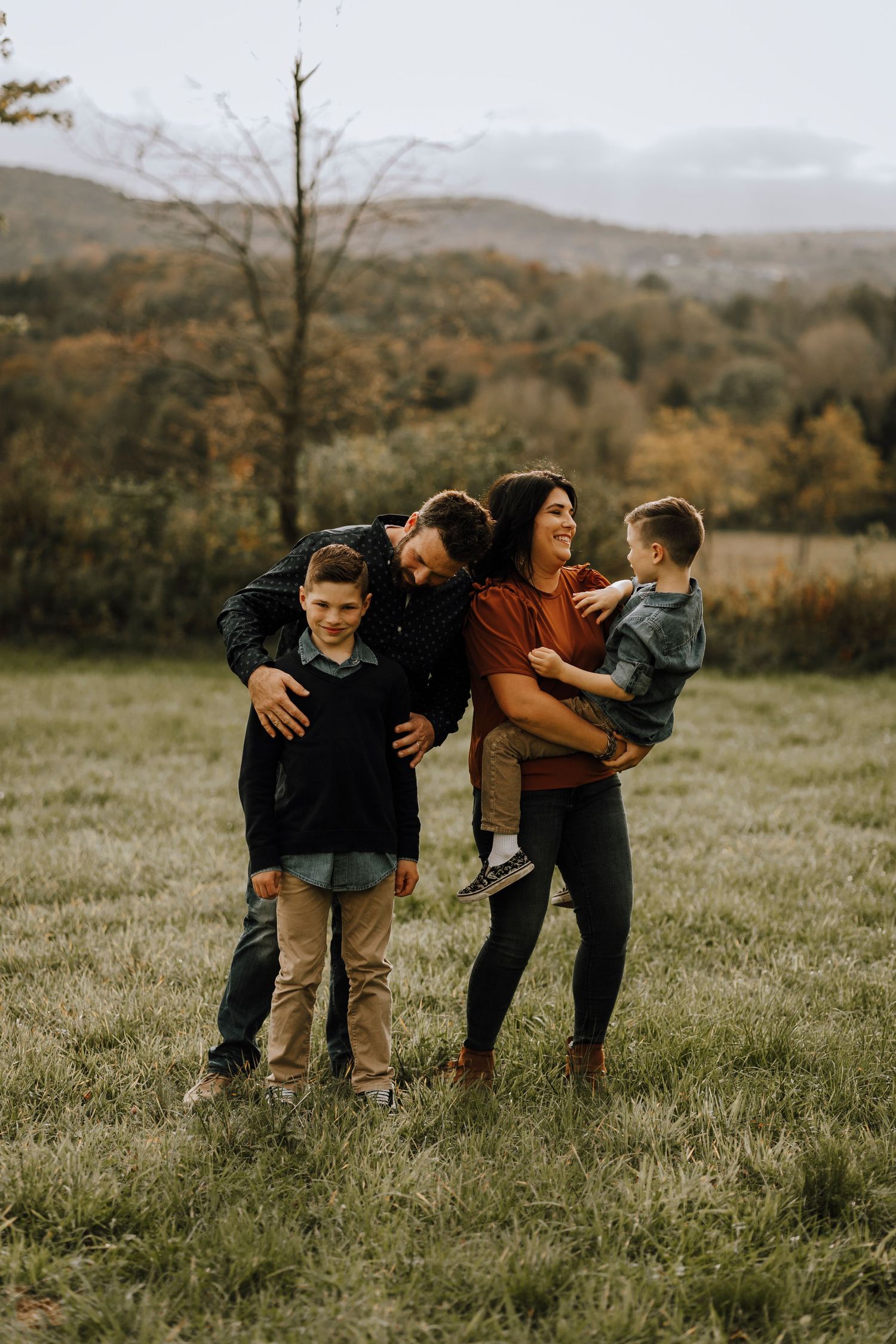 Family sharing a playful candid moment together on a grassy hillside with mountains in the background.