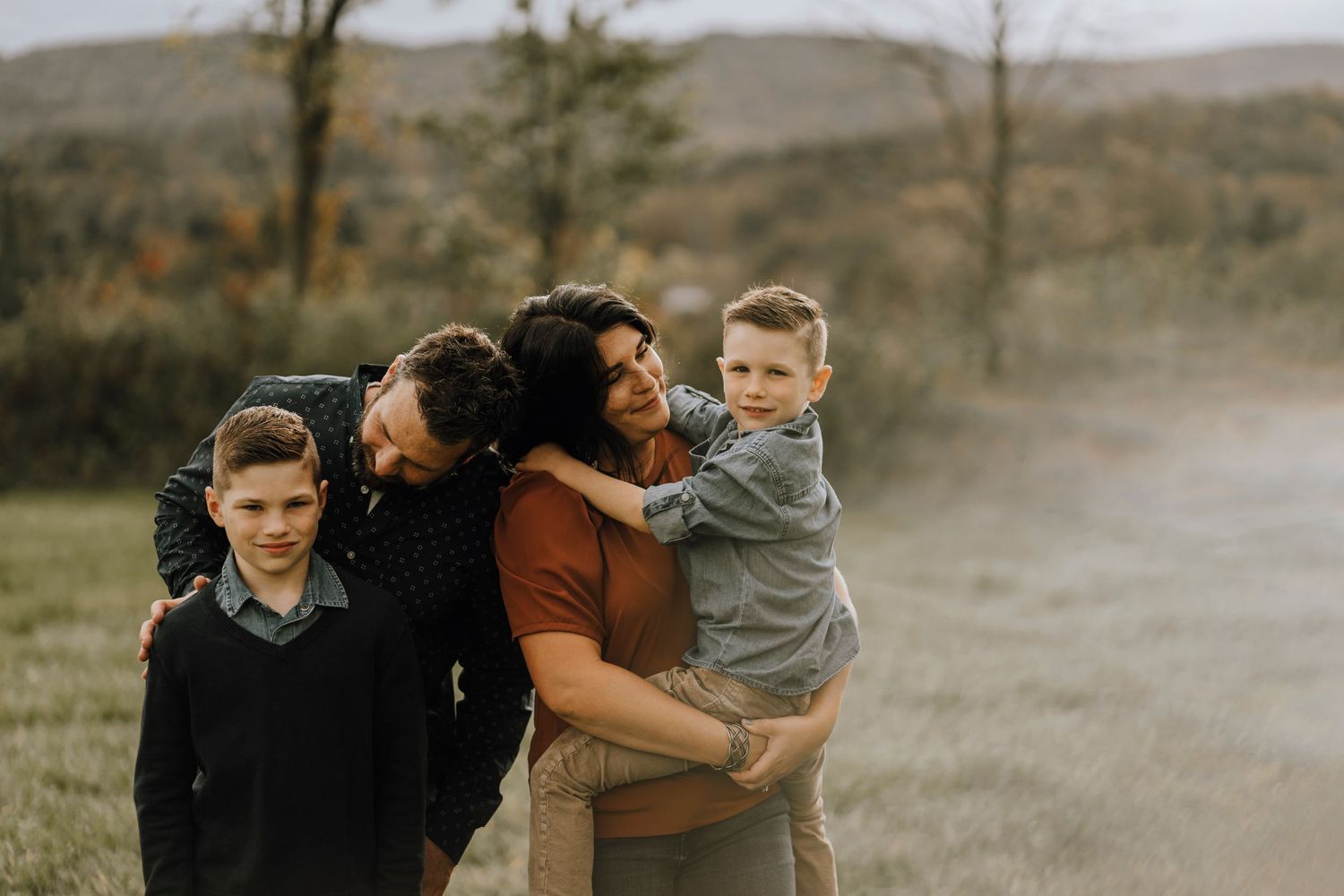 Candid family portrait showing affectionate interaction outdoors against mountain backdrop.