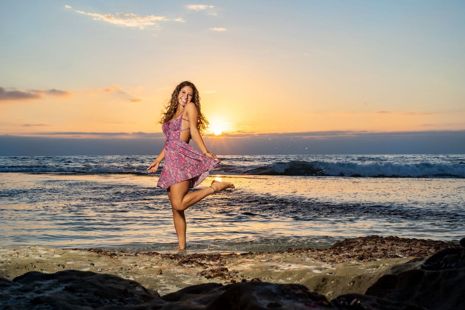 A high school senior silhouette dancing on beach at sunset wearing flowing dress.