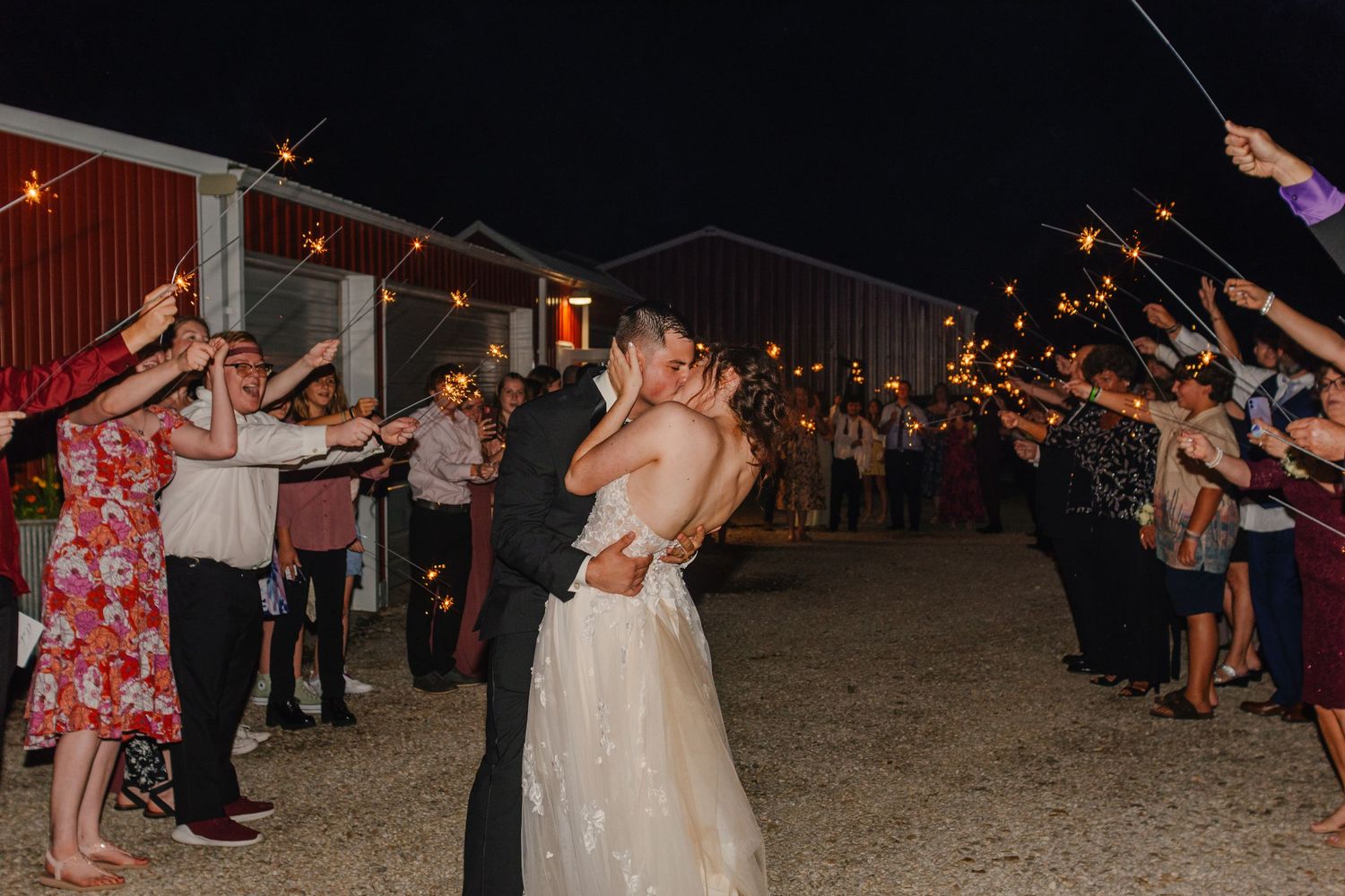Wedding guests form a sparkler exit line at night for celebrating newlyweds.
