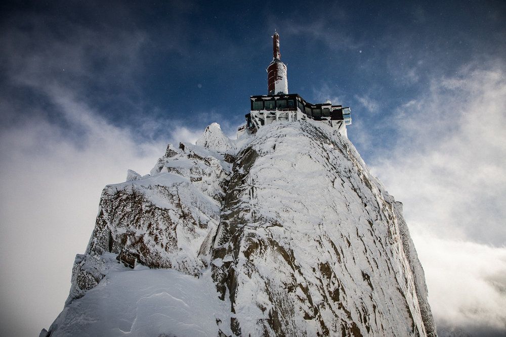 A snow-covered mountain peak with an observatory building perched dramatically at its summit.