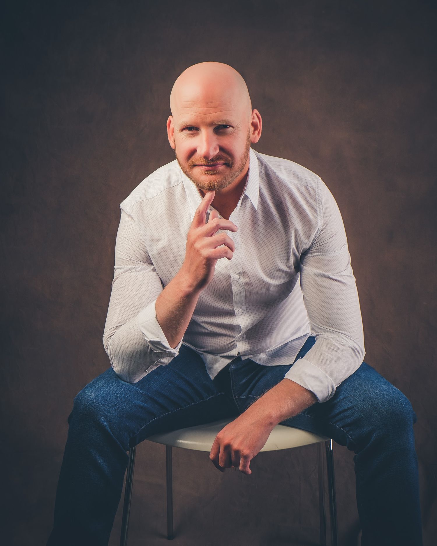 Person in white shirt and jeans sitting thoughtfully on a dark background.
