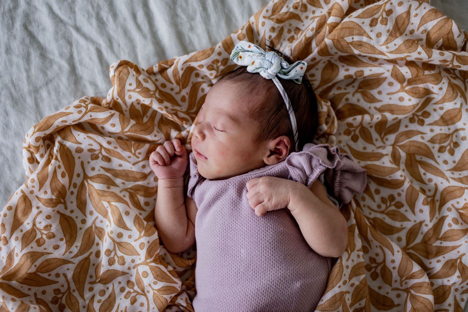 Sleeping newborn wearing pink clothing on a beige floral blanket.