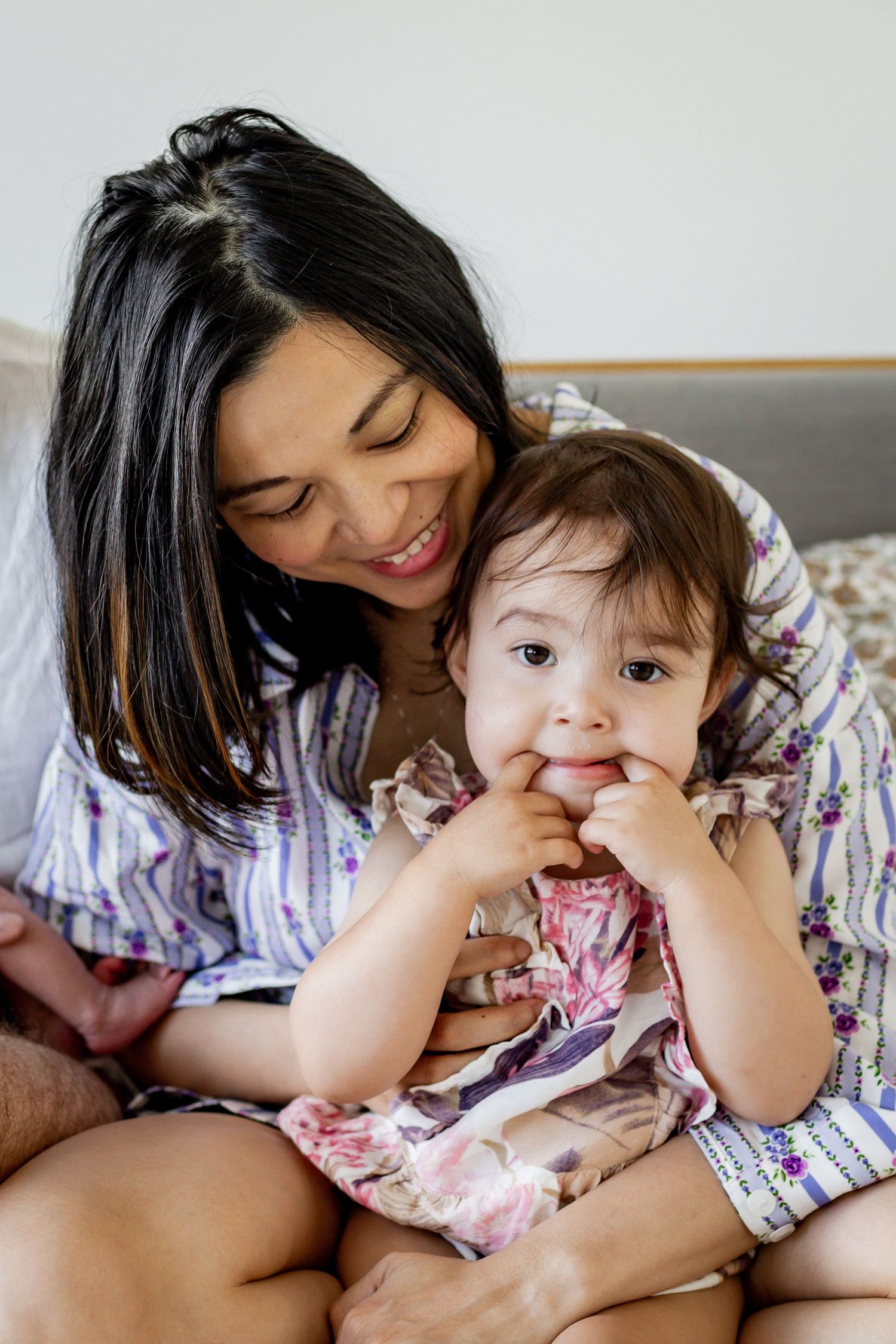 Mother and child sitting together on grey couch in matching floral outfits.