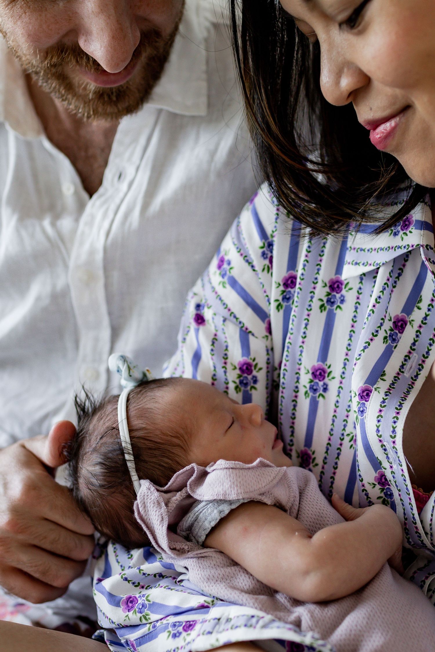 Close up of sleeping infant in pink clothing being held by adults.