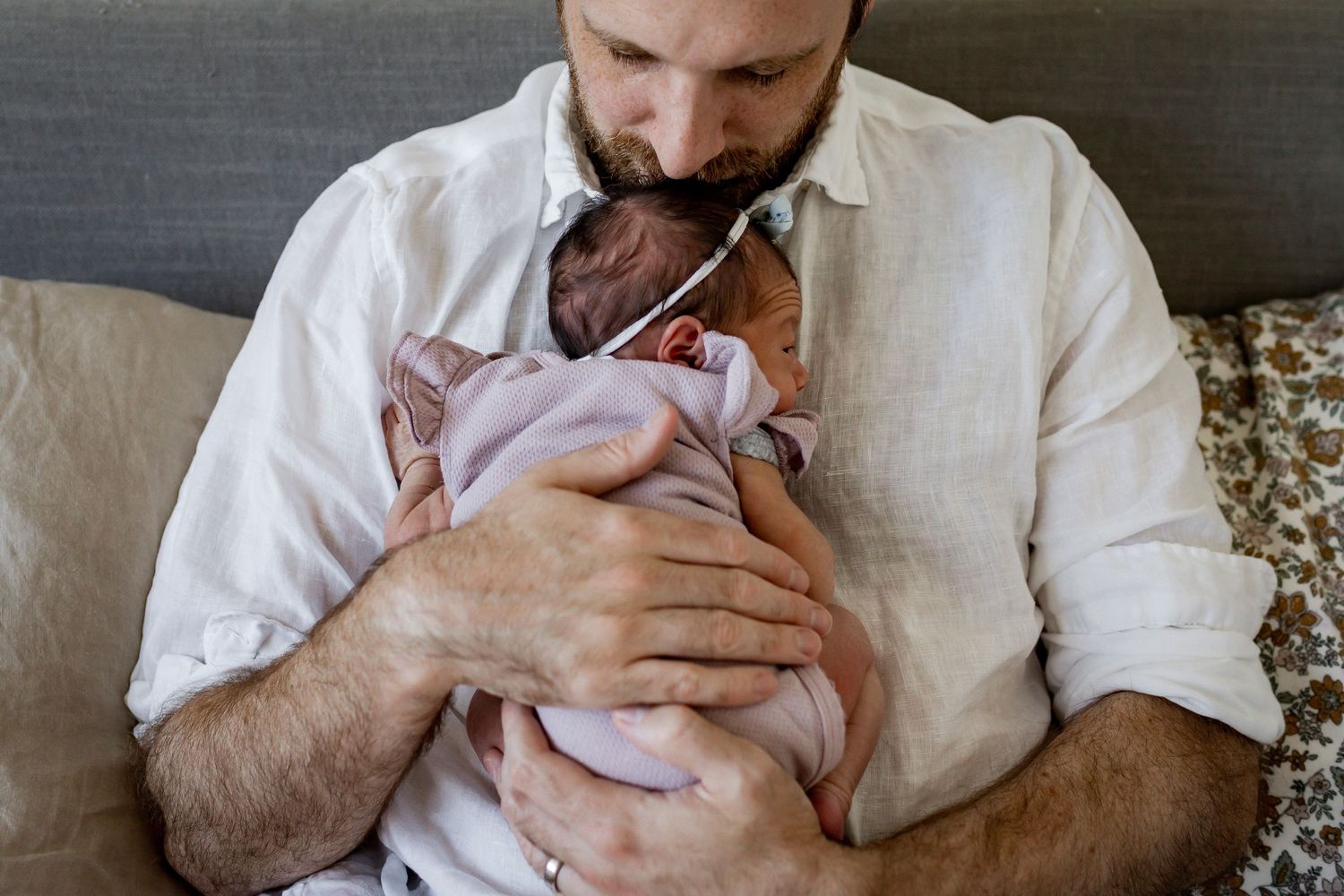 Person in white shirt holding sleeping infant wrapped in pink clothing.
