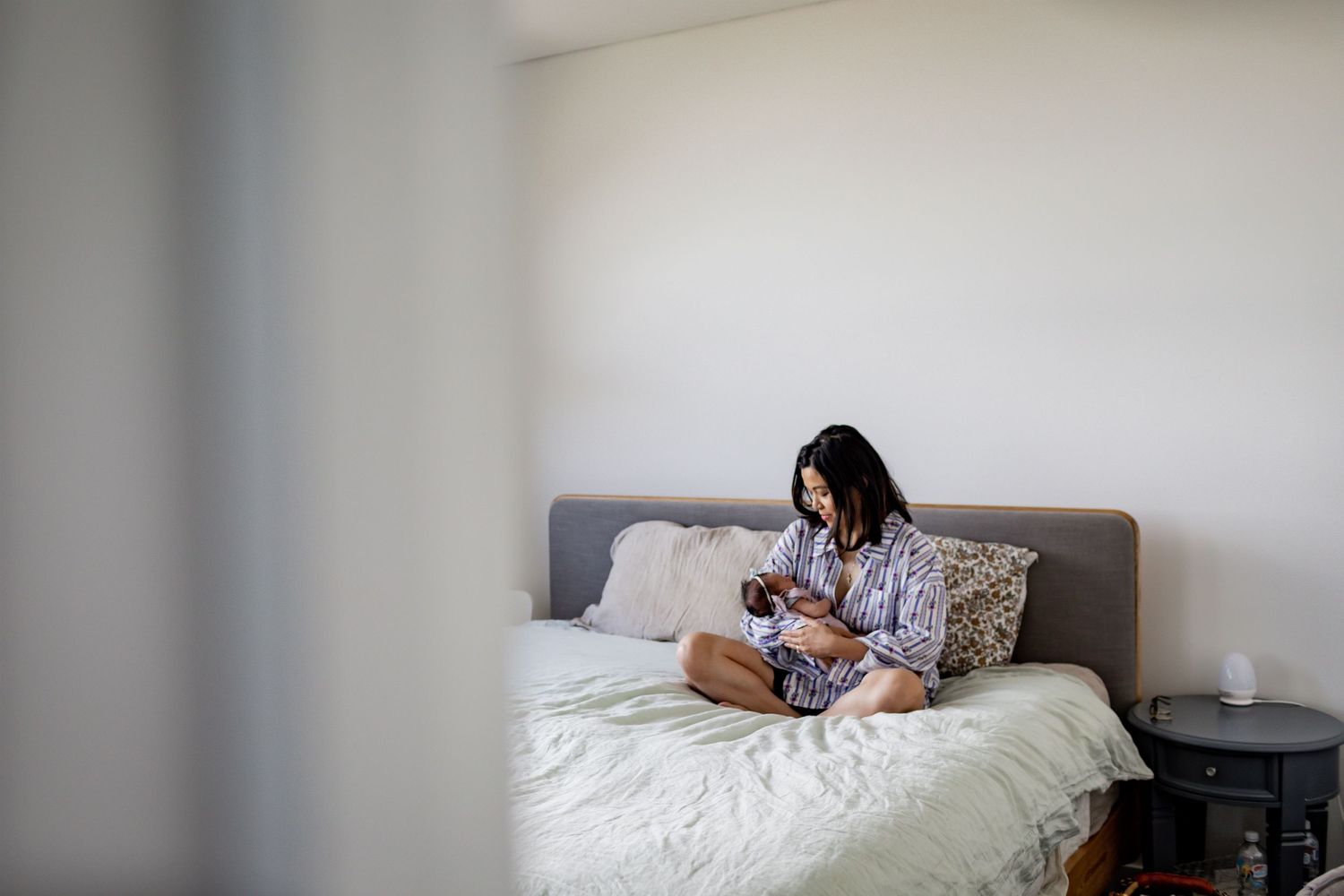 Person in pajamas sitting on bed while looking at smartphone in minimalist bedroom.