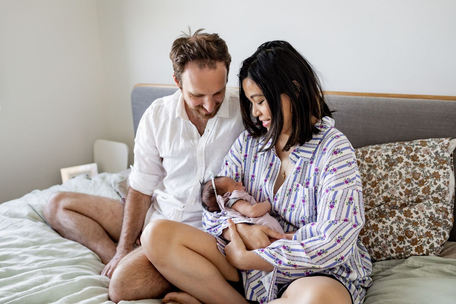 Family sitting together on grey bedding while looking down at something.