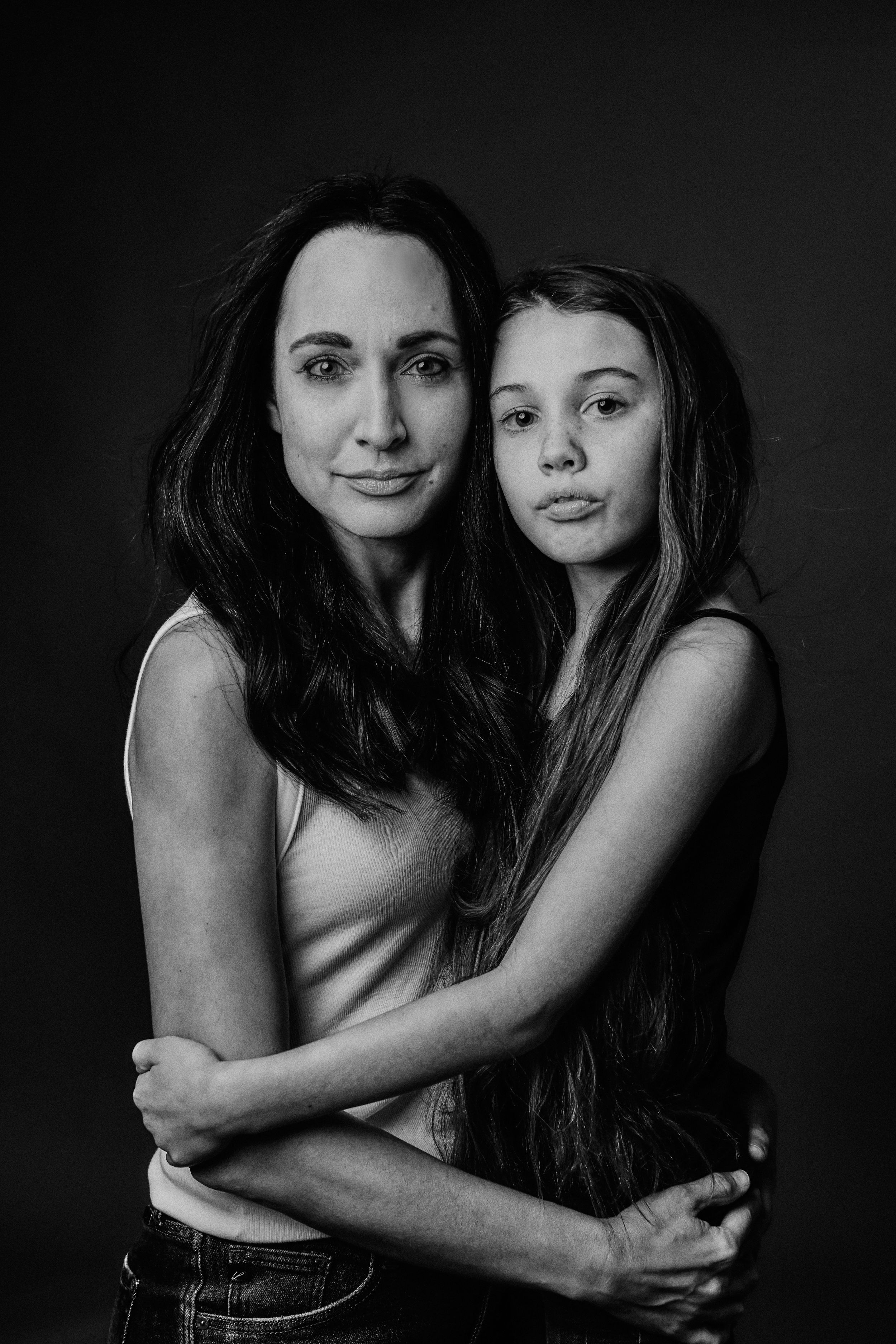 Intimate black and white portrait series of two women embracing against dark backdrop.