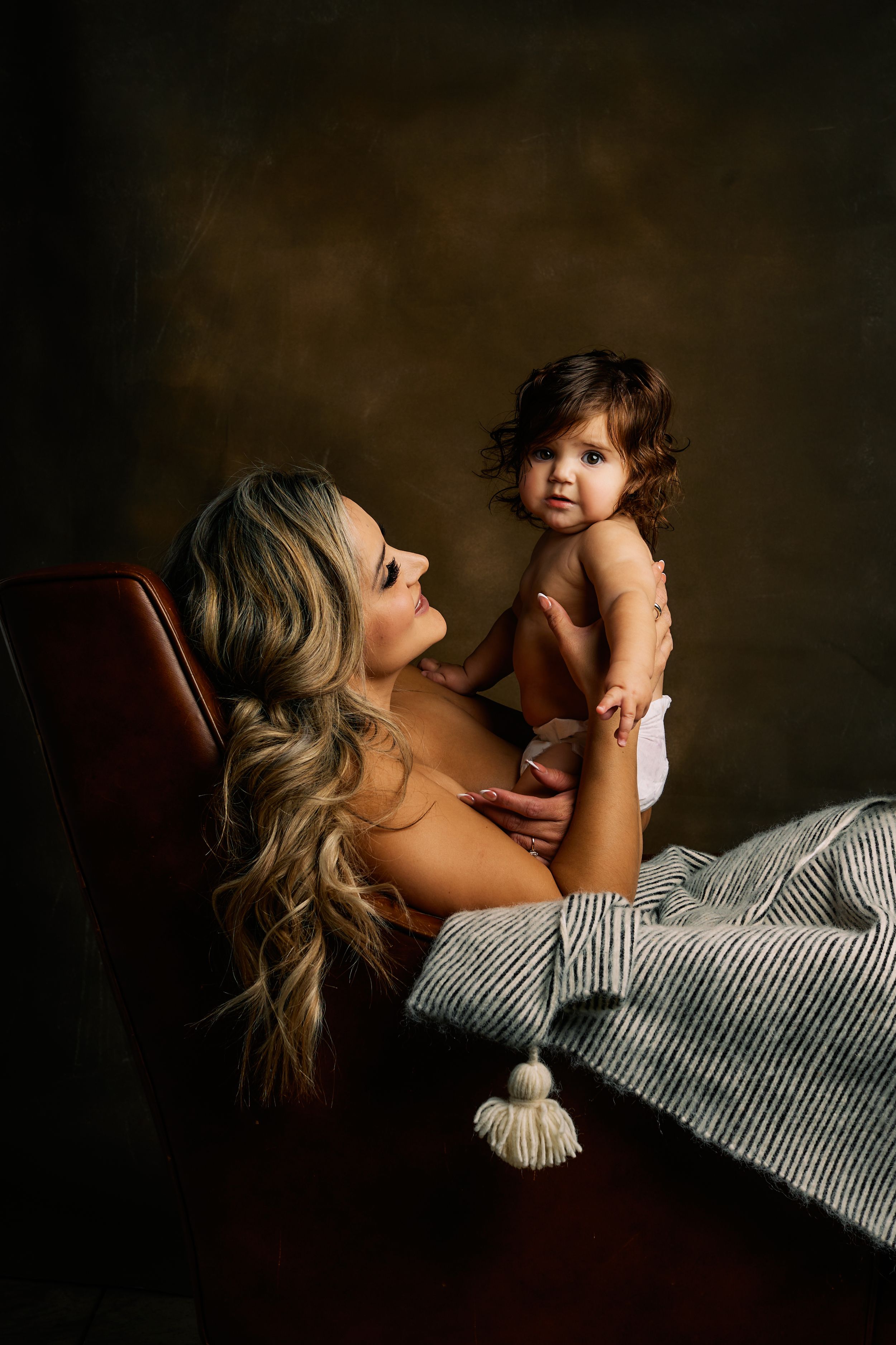 Intimate lifestyle portrait of parent and baby in warm dramatic lighting.