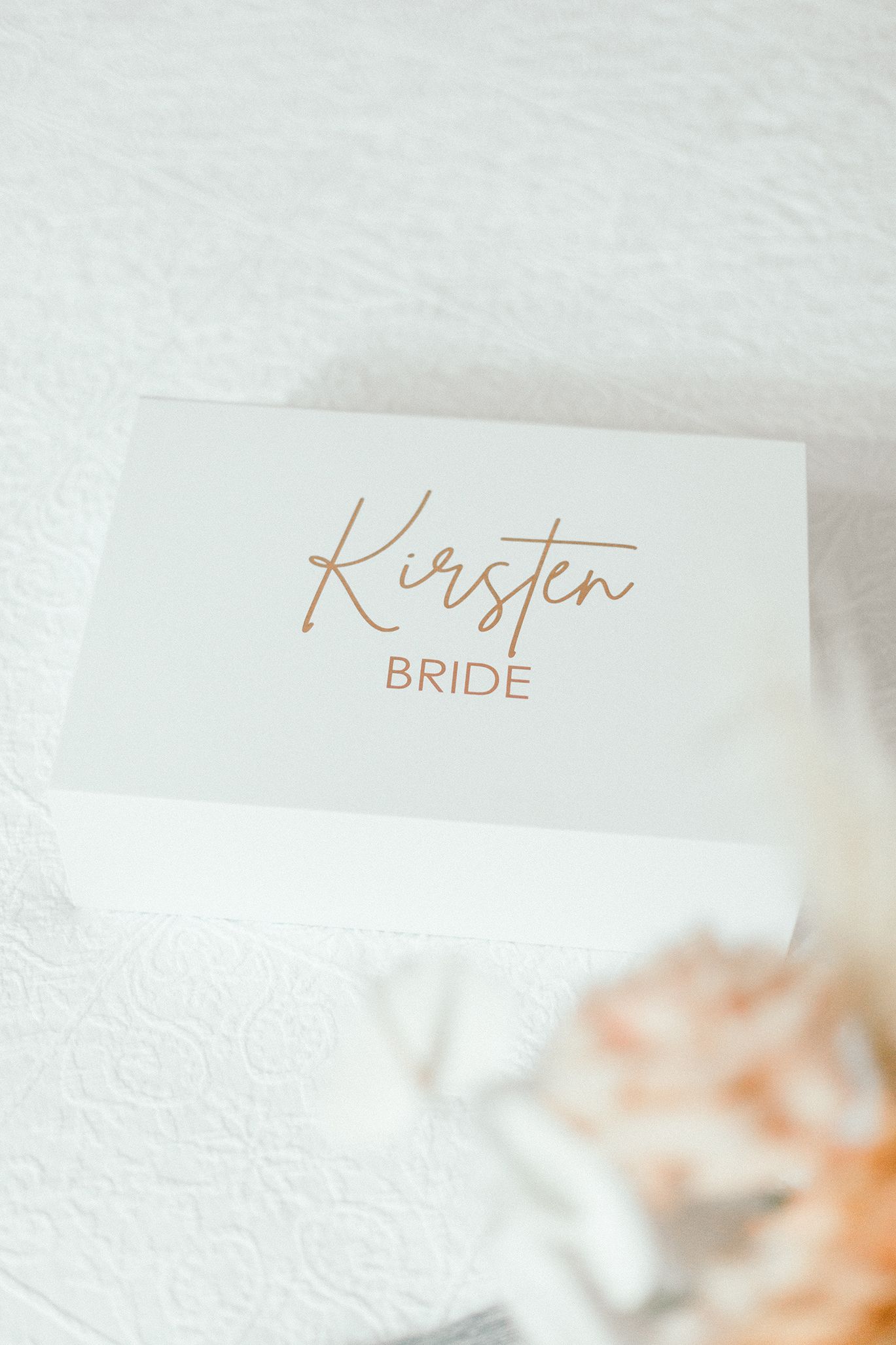 White place card with 'Kirsten Bride' written in elegant rose gold calligraphy script.