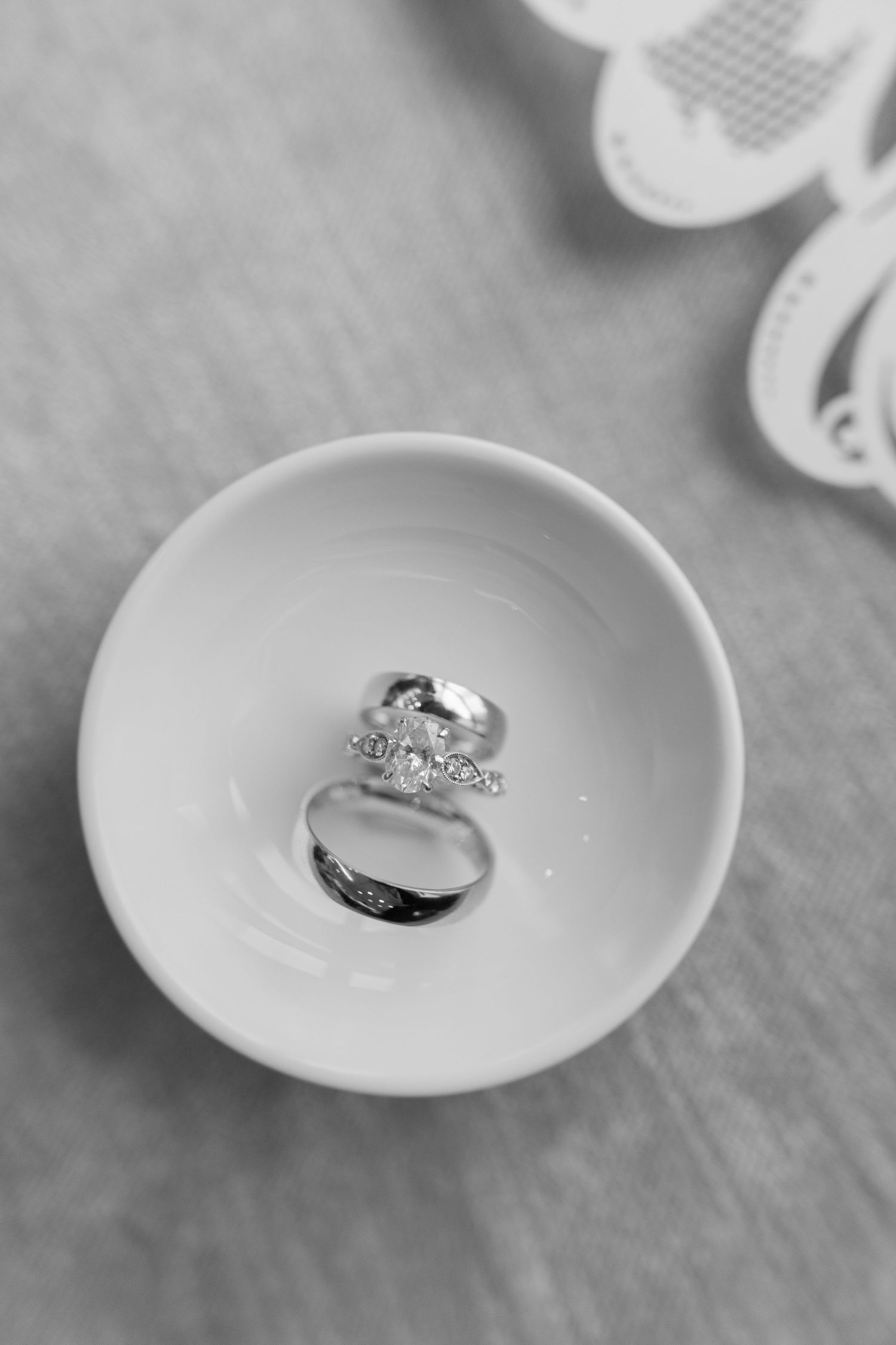 Wedding rings nestled in a small white ceramic bowl captured in black and white.
