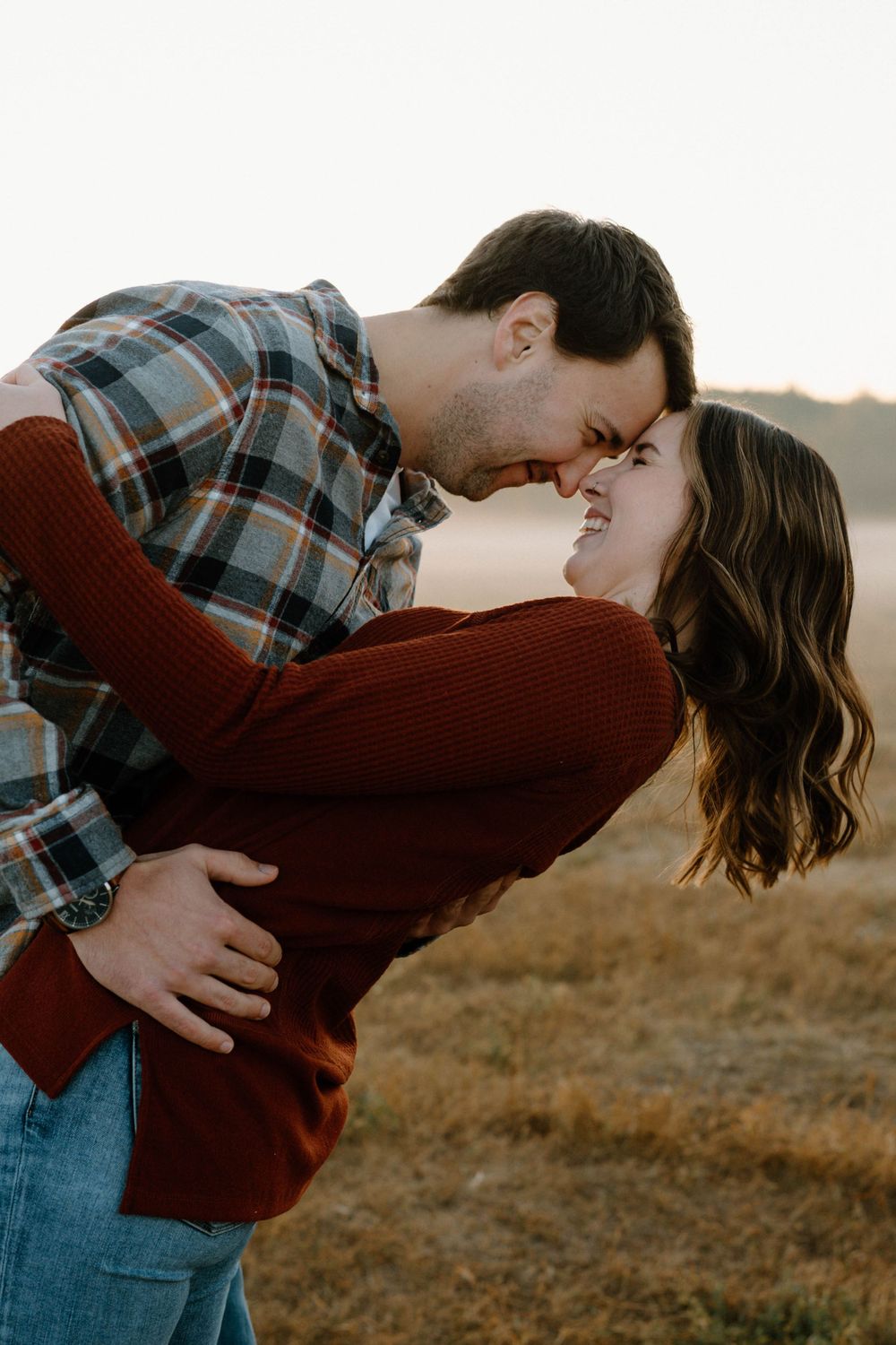 A romantic dip kiss captured in warm light on a misty field.