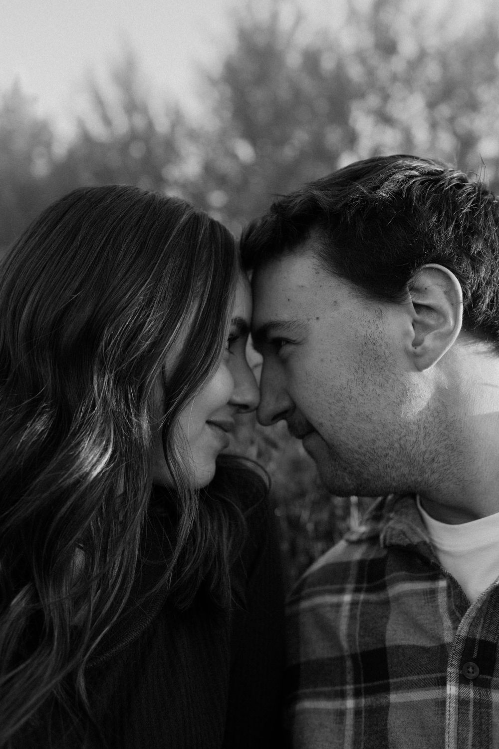 A close-up black and white portrait of a couple sharing an intimate moment outdoors.