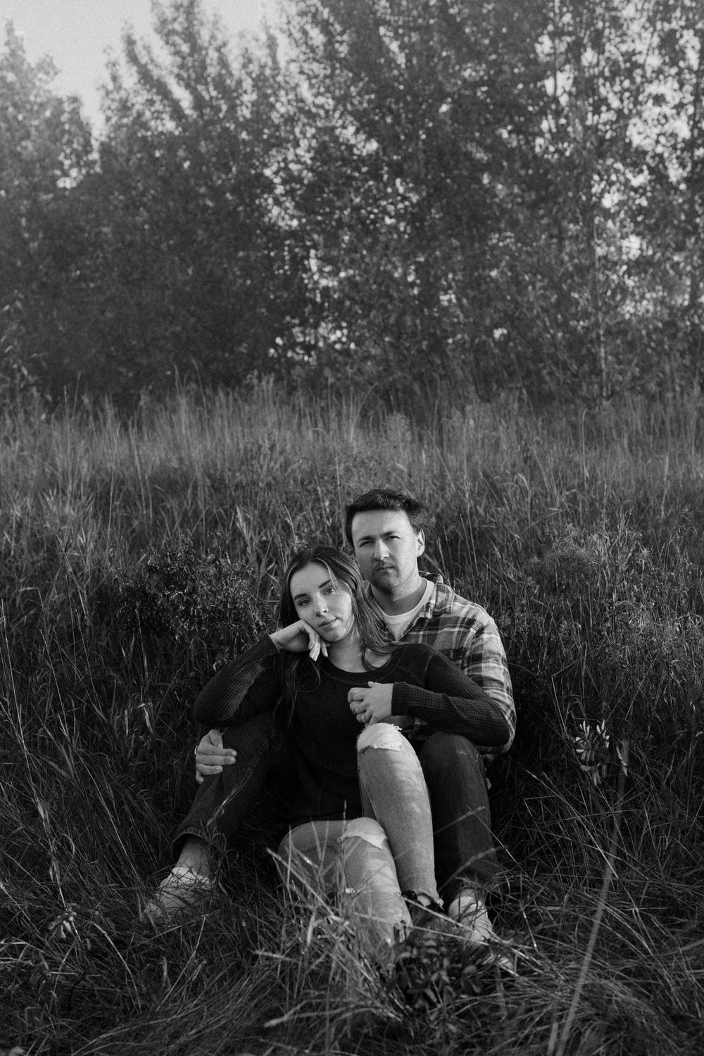 Black and white portrait of two people relaxing in a grassy field.
