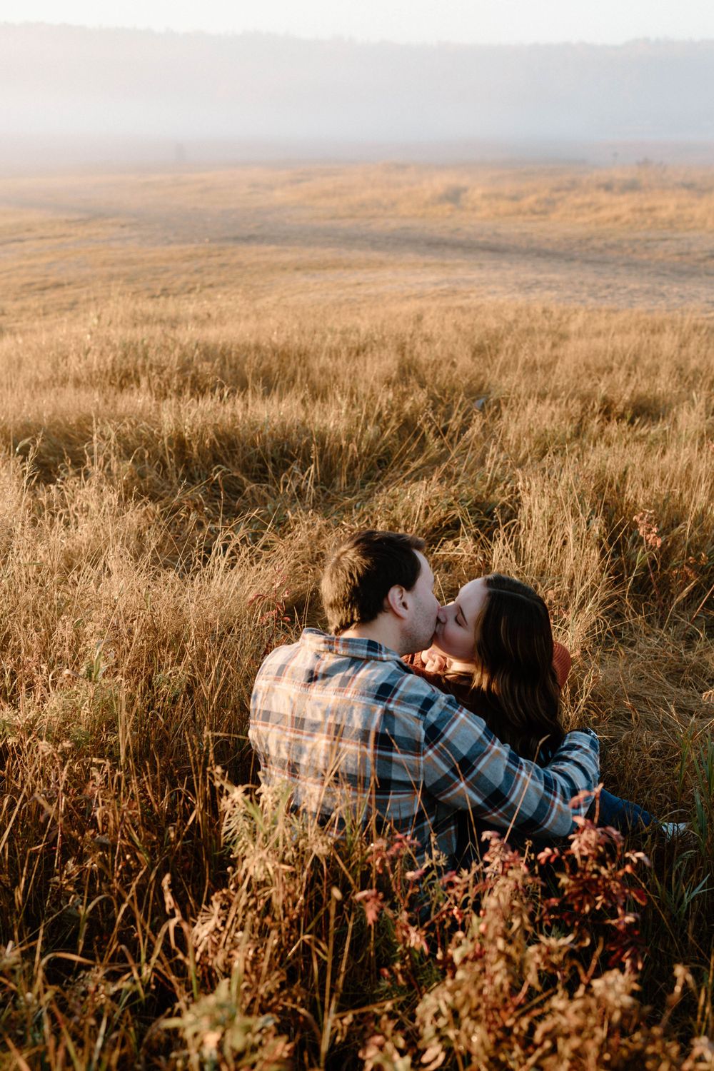 Couple sharing an intimate moment in a vast golden prairie landscape.