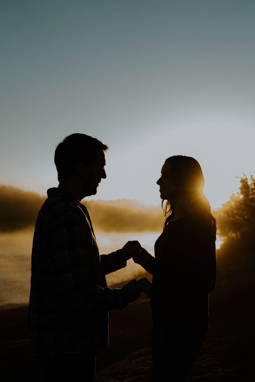 Dramatic silhouette of two people in a touching moment against a sunset sky.