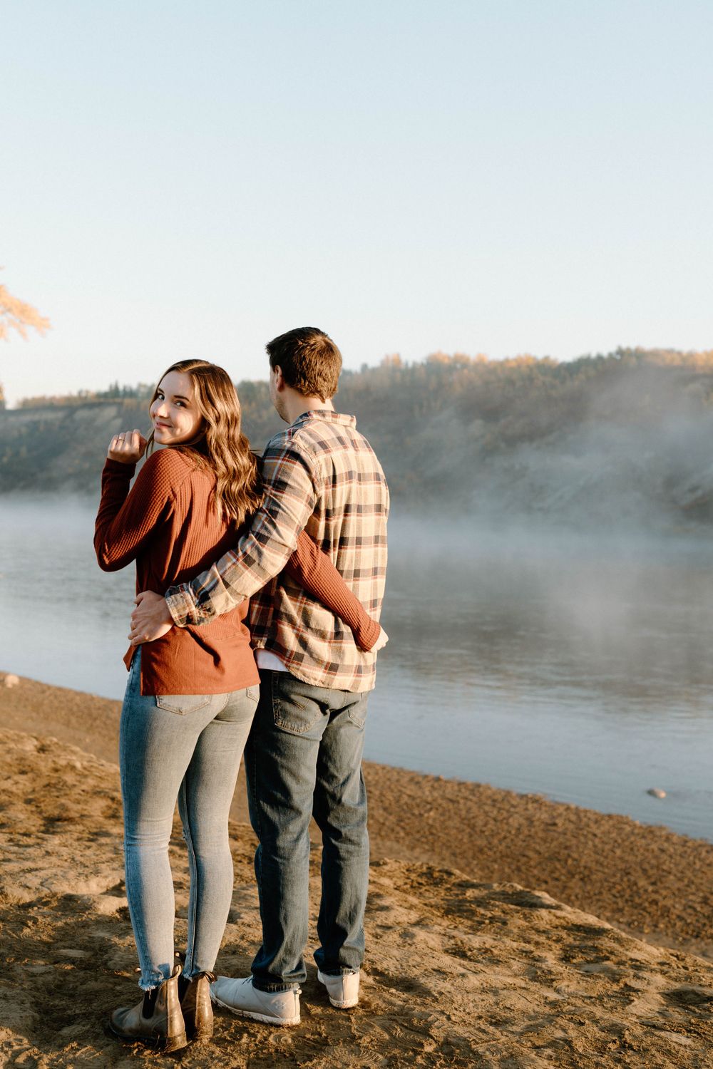 A couple walking together along a misty lakeshore at sunrise.