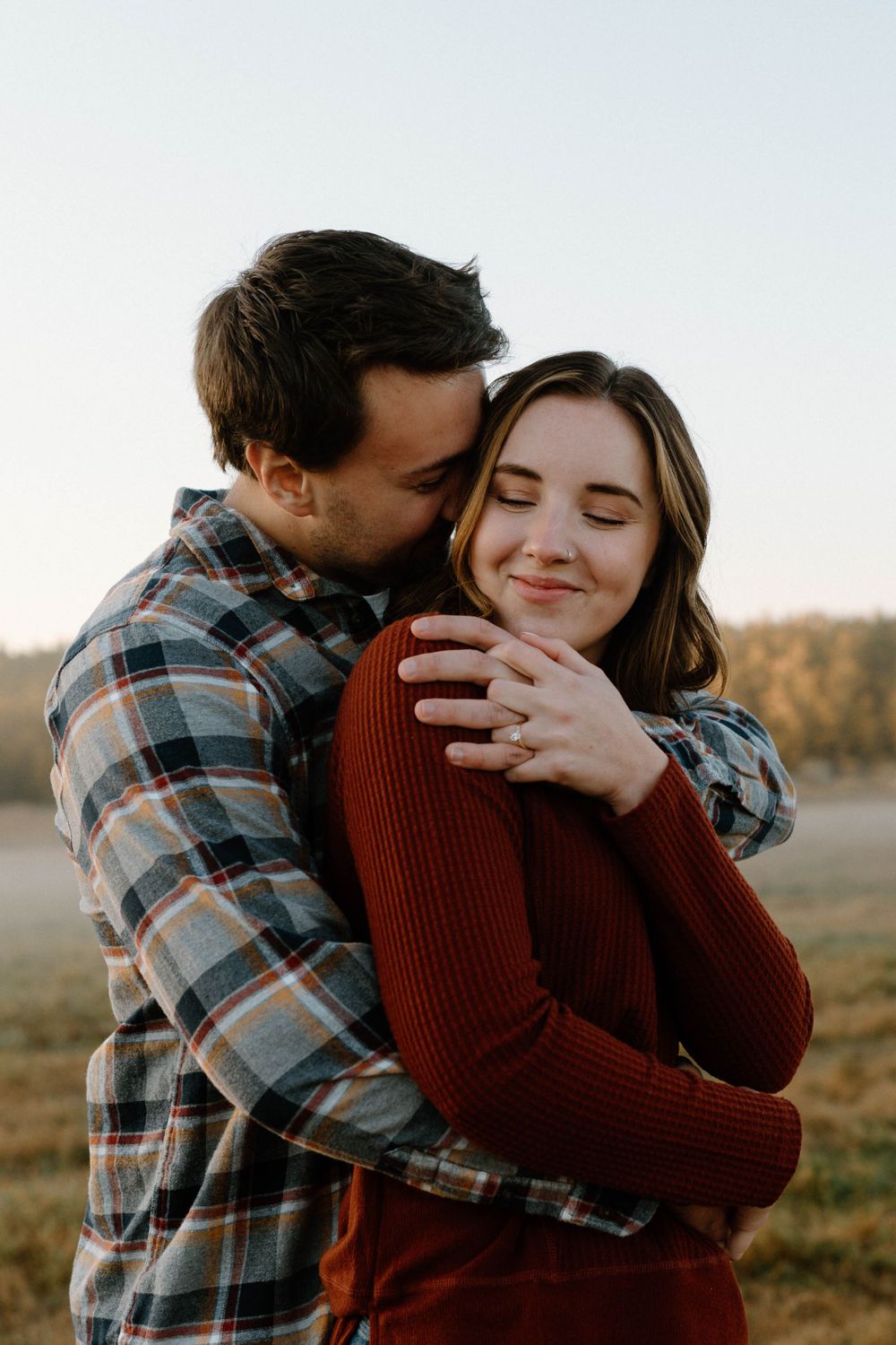 A romantic embrace between two people in casual wear standing in a golden field.