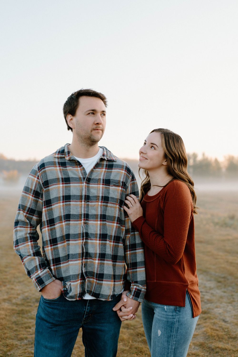 Romantic couple poses in a foggy field during sunrise while holding hands.