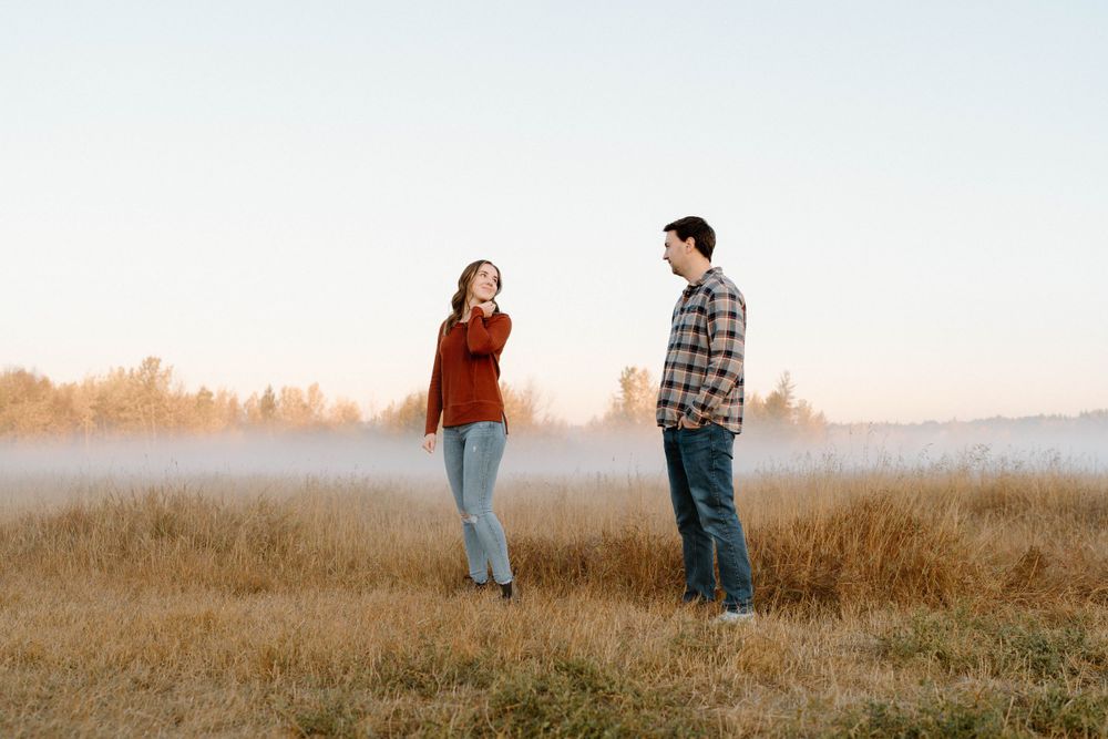 Couple sharing a candid moment while standing in a misty field at dawn.