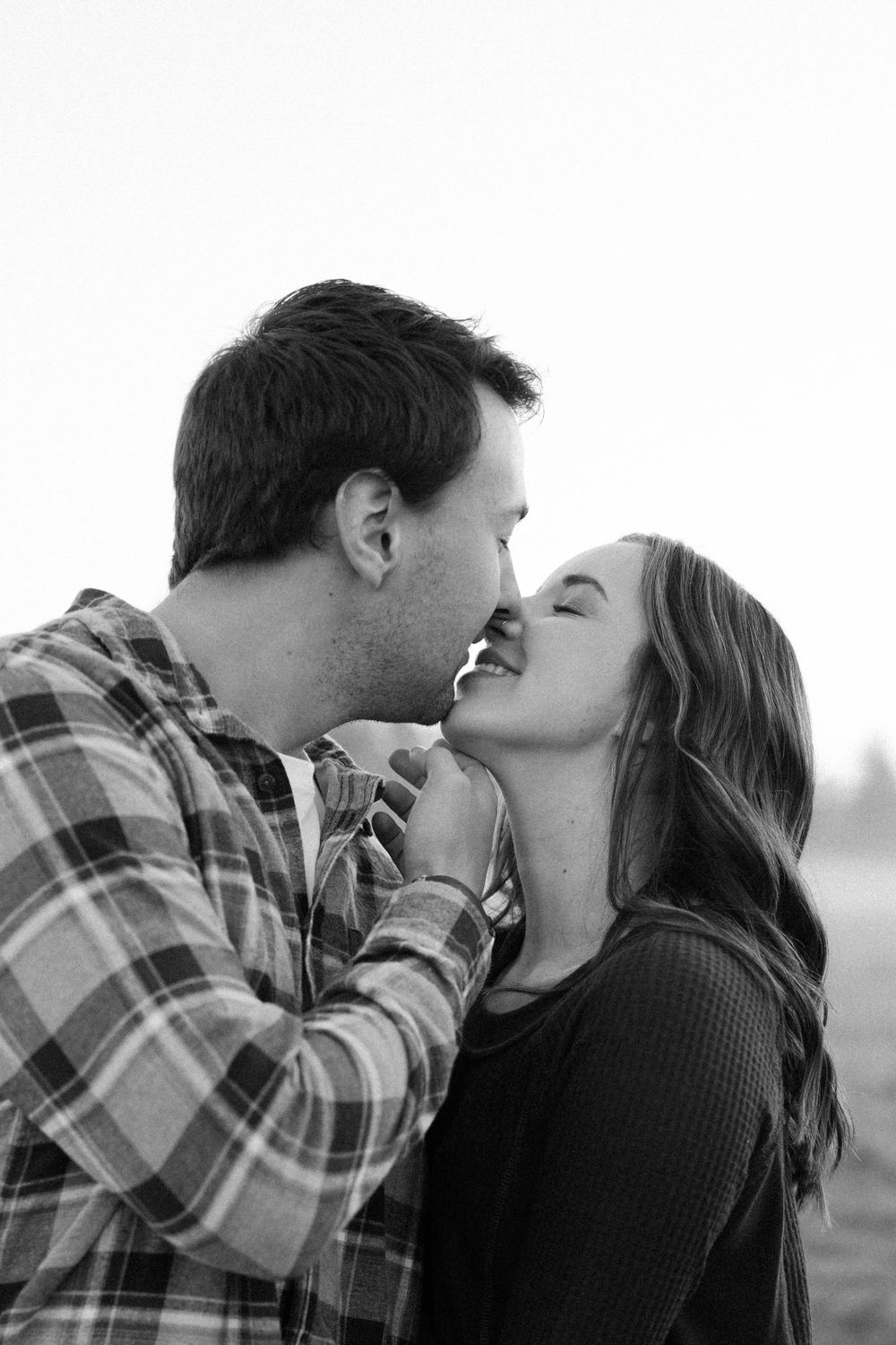 A romantic black and white photo series of a couple kissing in a field.