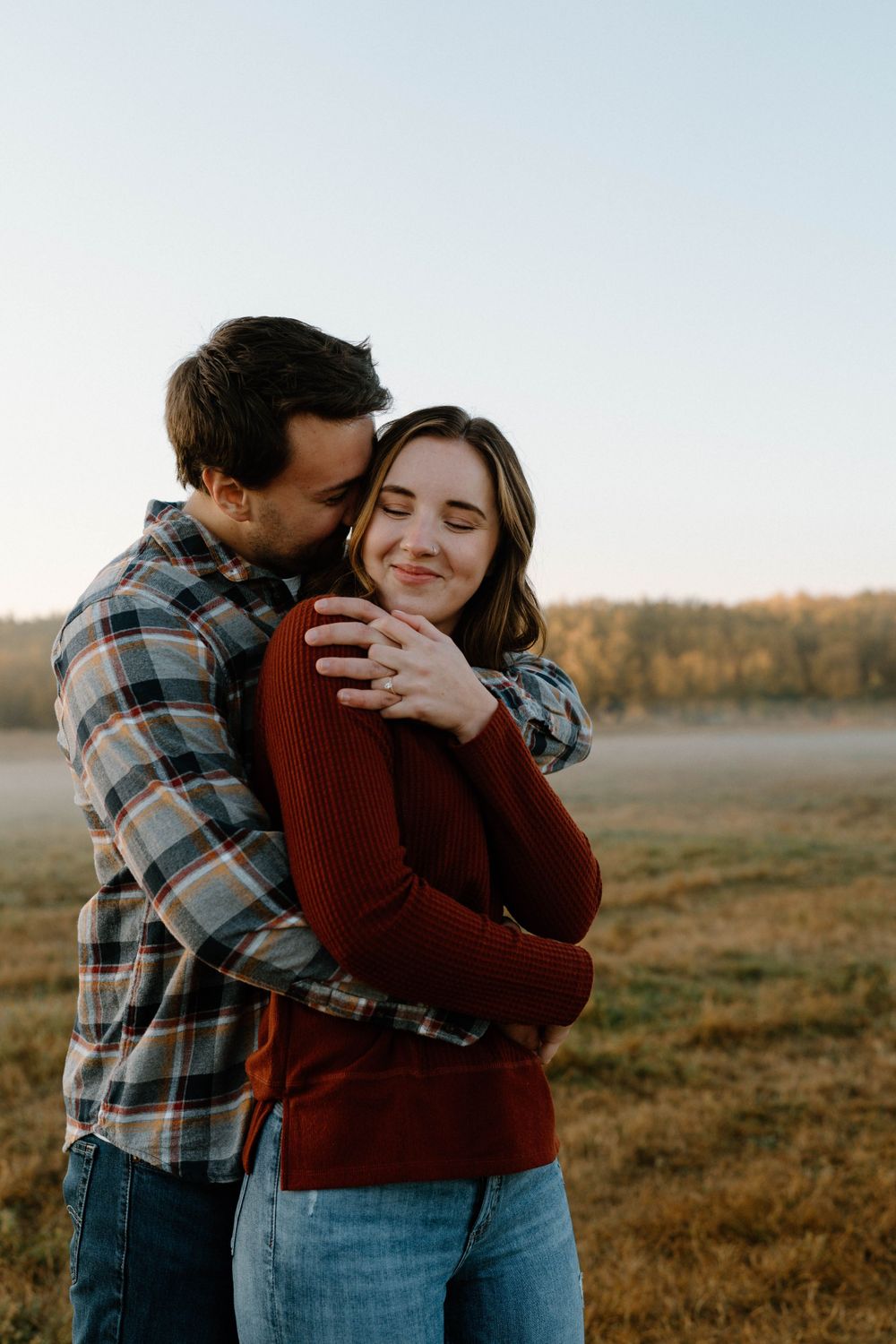 A tender moment between a couple hugging in an autumn field at dusk.