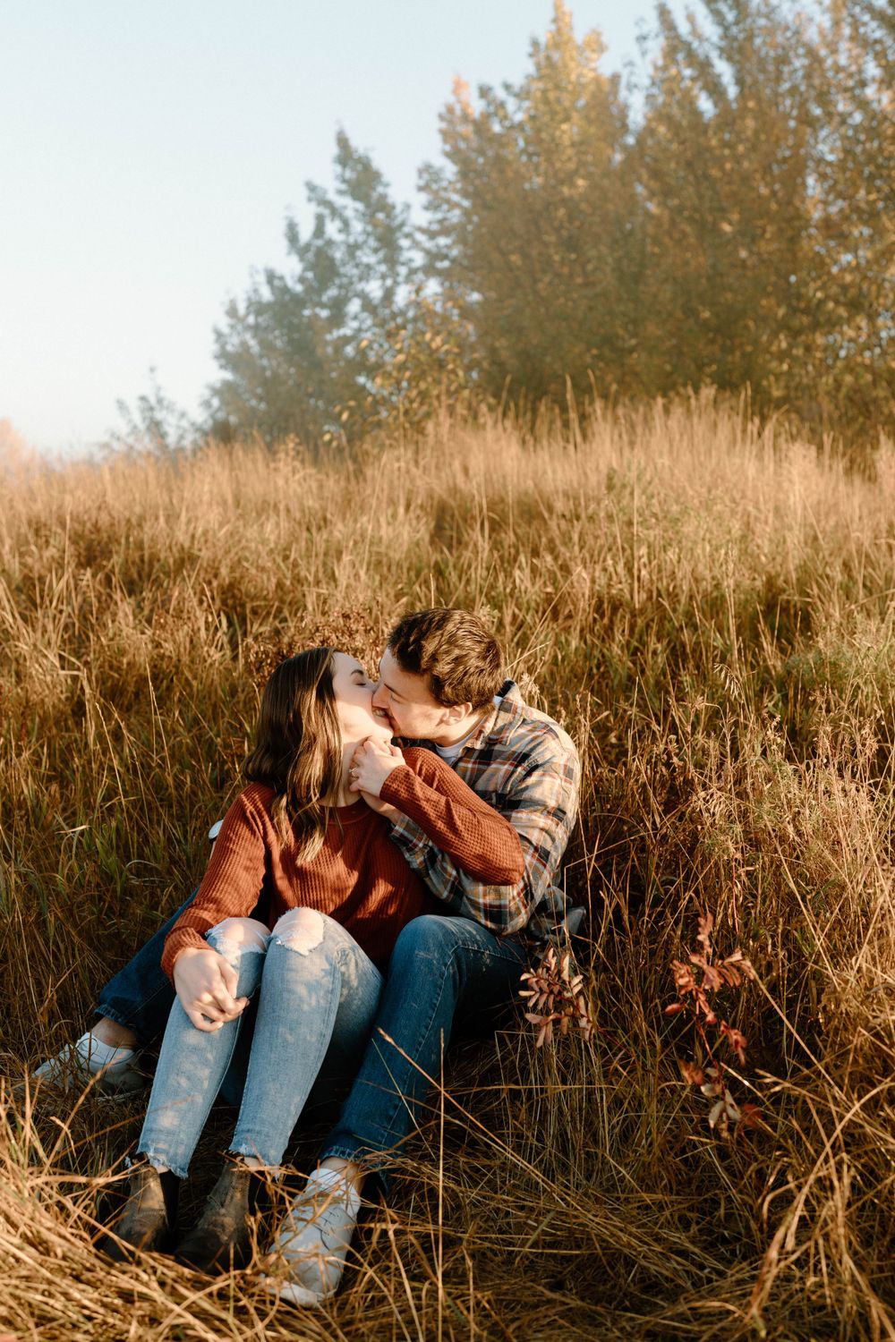 Sun-kissed couple resting in tall autumn grass during golden hour.