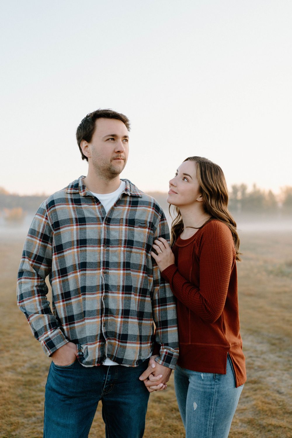 Couple in casual attire sharing a tender moment in a misty morning field.