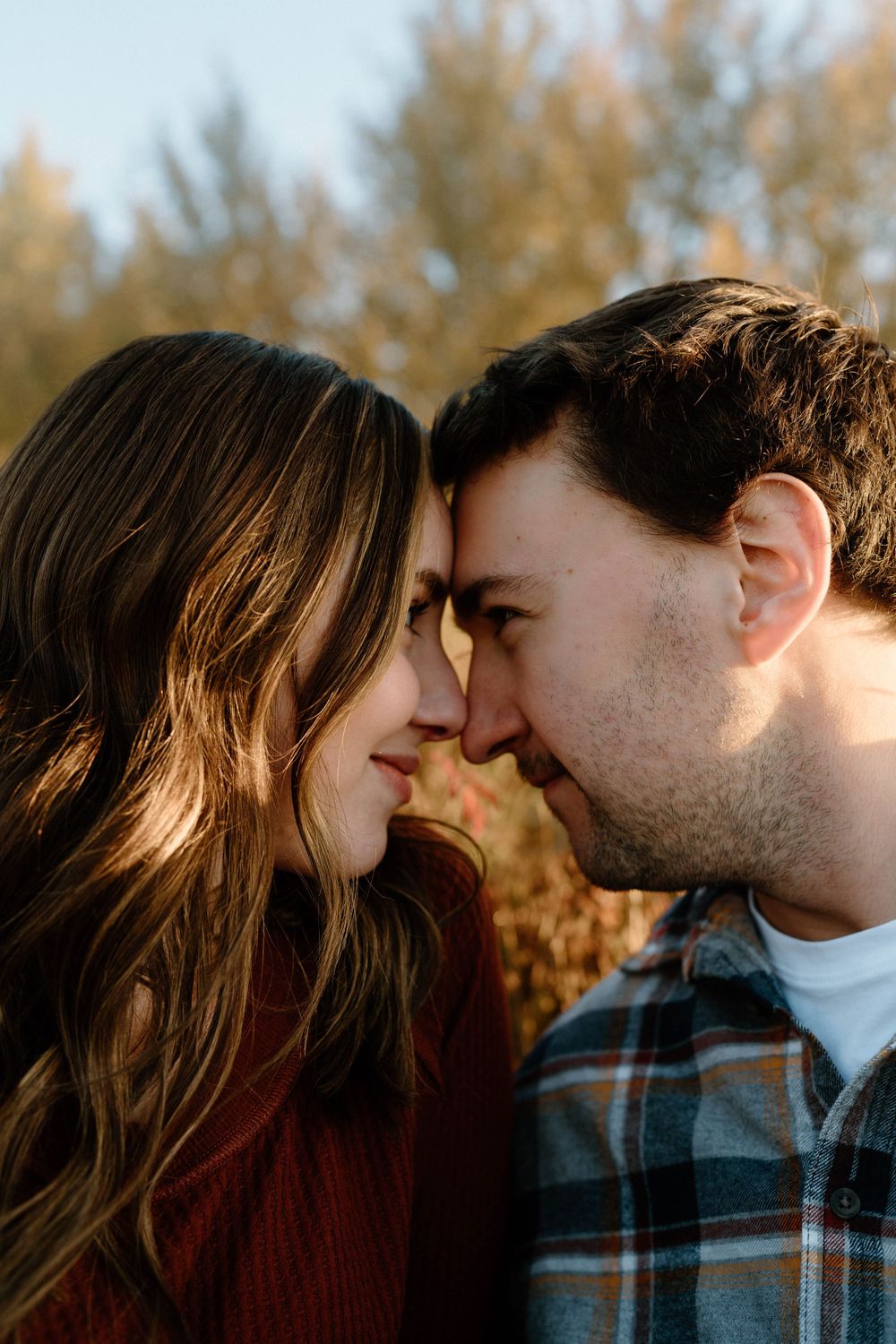 A tender close-up moment between a couple during golden hour with autumn foliage in background.