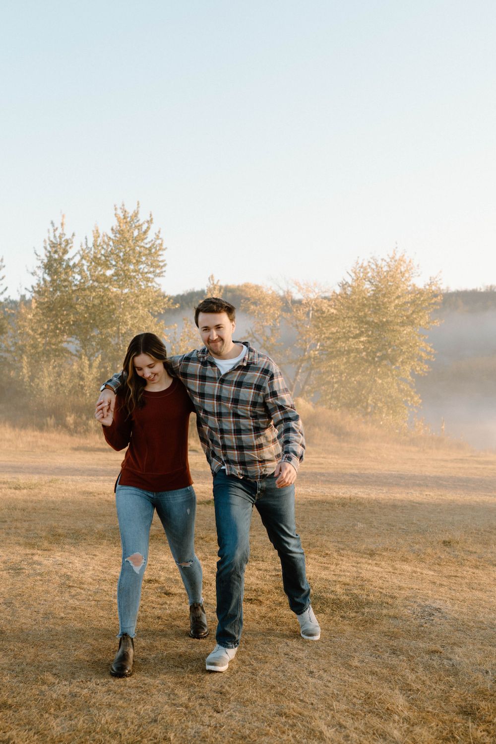 A playful couple walking together on a path during sunset with trees in background.