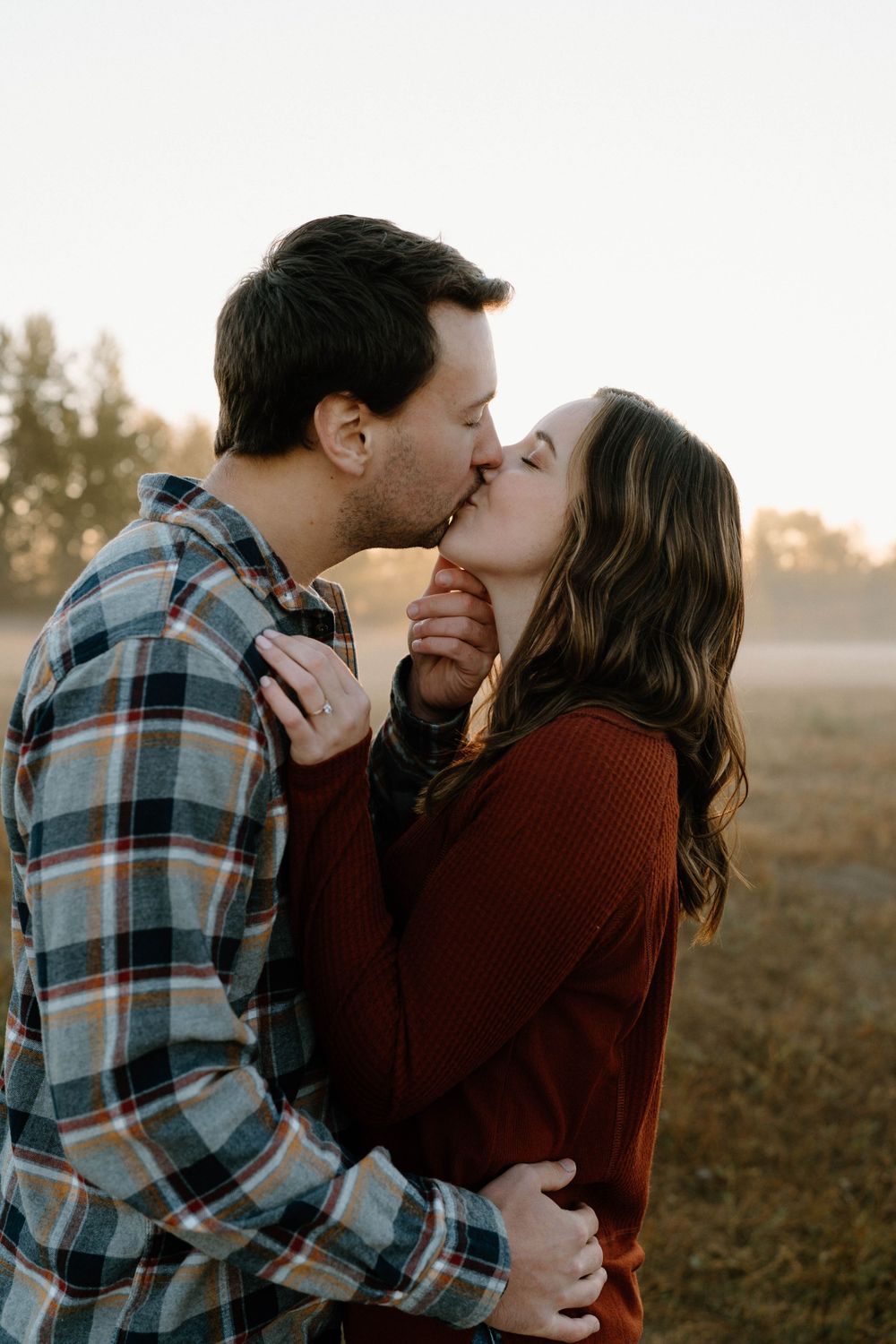 An intimate moment shared between a couple kissing in a misty outdoor setting.