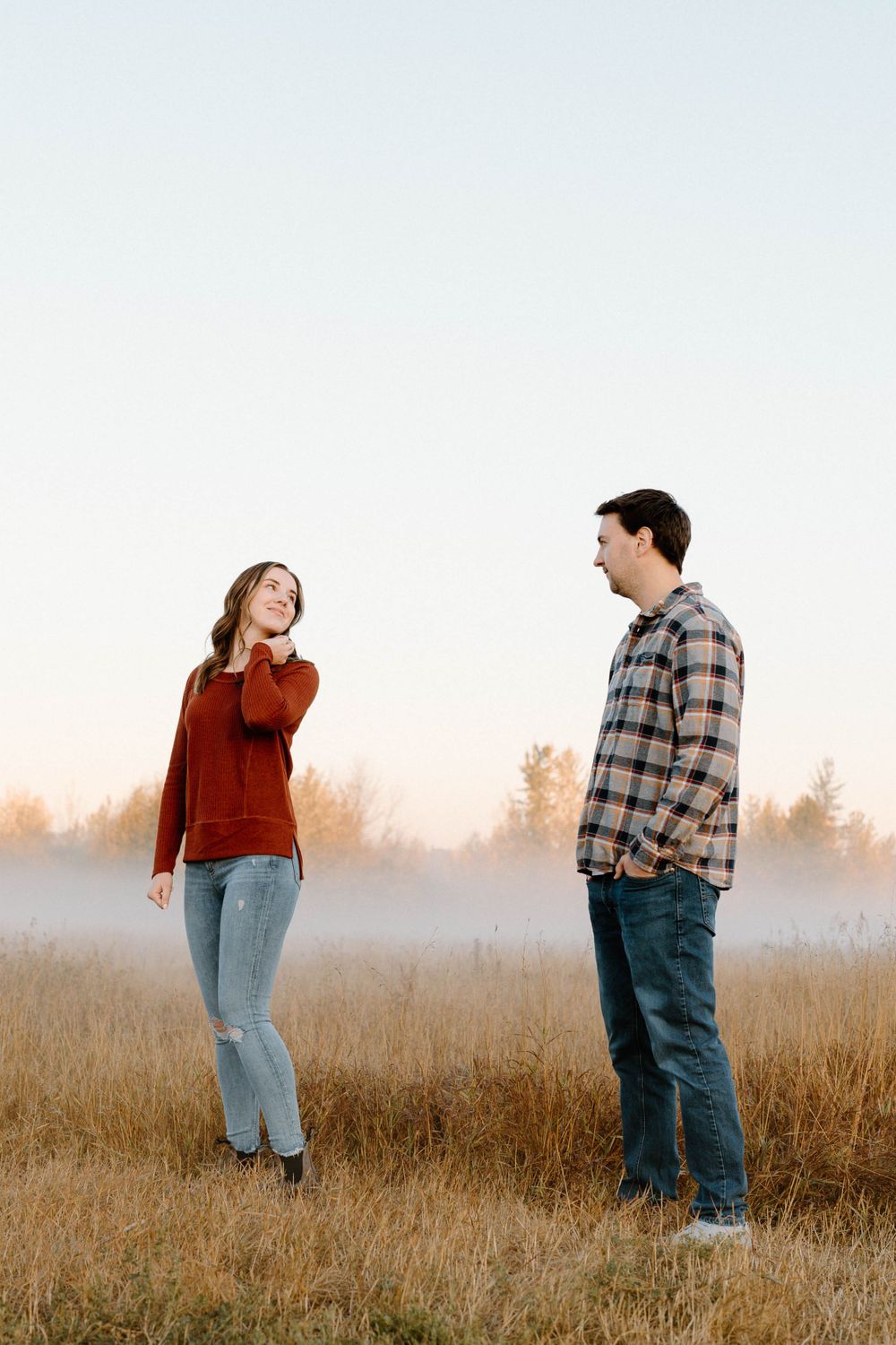 Playful couple standing in a golden field with morning mist in the background.