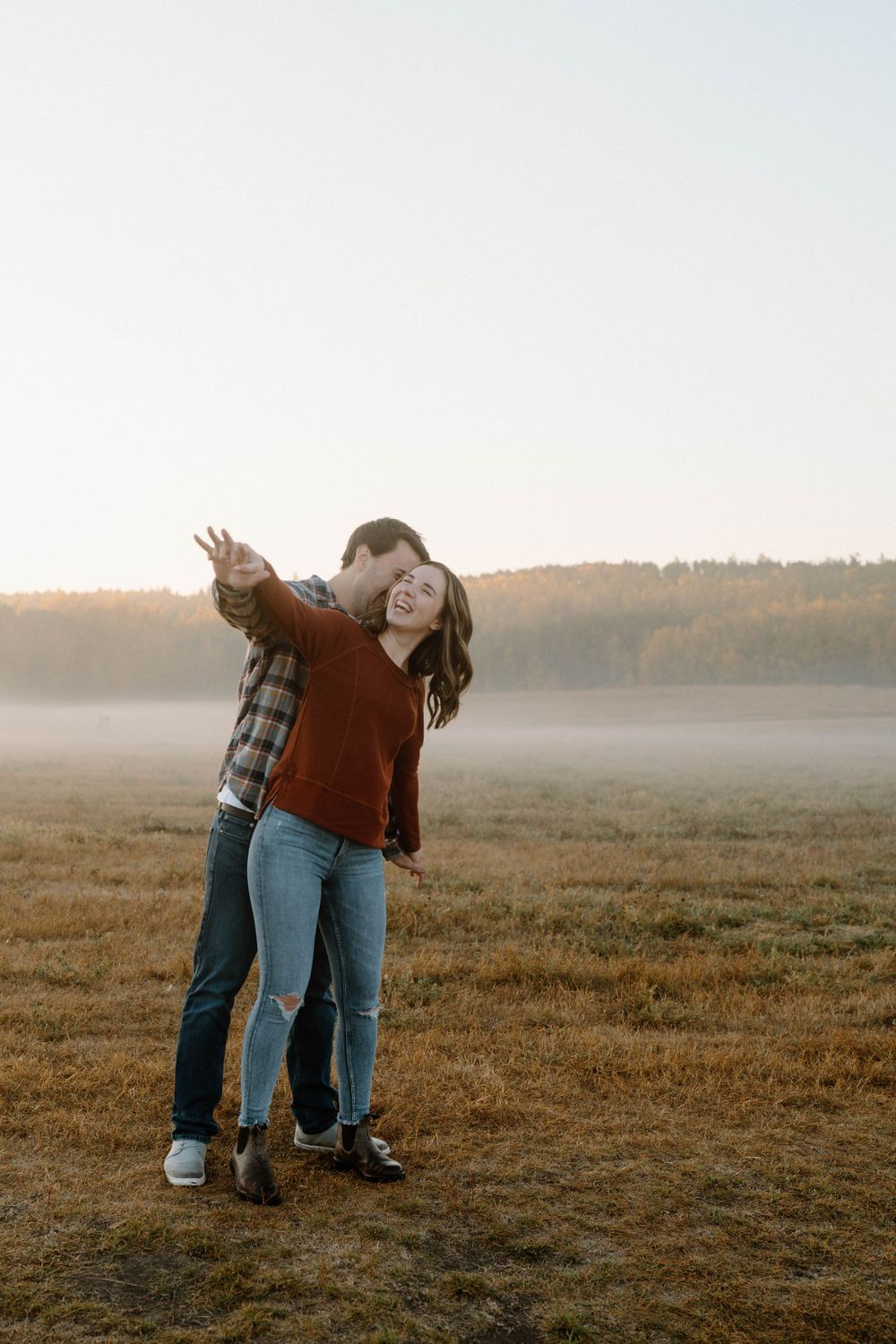 A joyful couple dances and embraces in a foggy field at sunset.