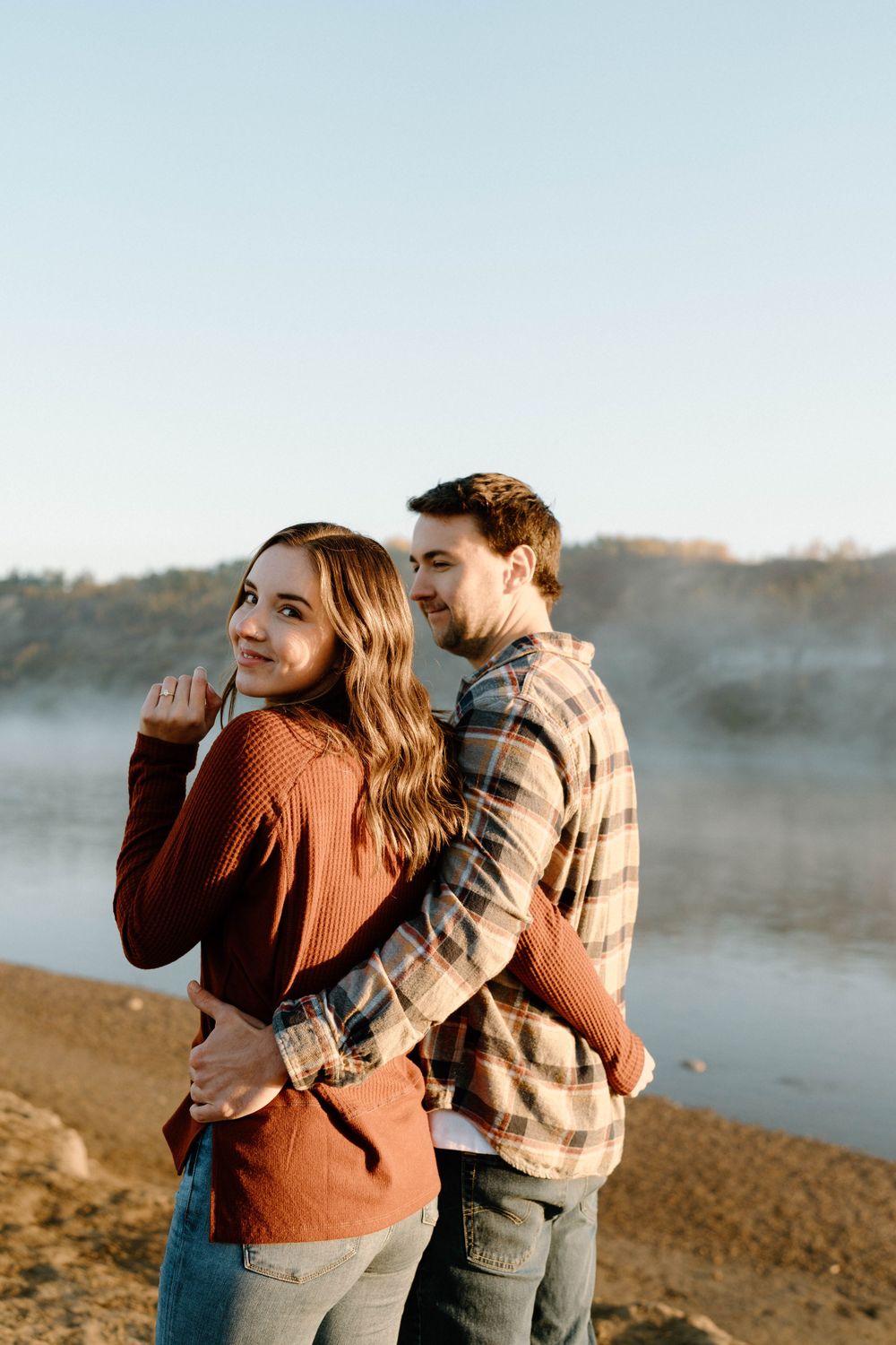 A couple shares laughter while standing against a foggy lake backdrop.