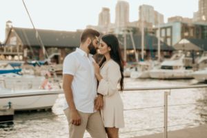 Romantic scene at marina with boats and city buildings in background during golden hour.