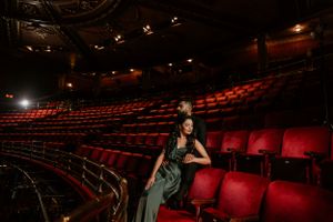 Empty theater auditorium with curved rows of red seats and dramatic lighting in the background.