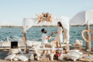 Decorated boat deck proposal scene with white fabric arch, flowers, and pillows over ocean waters.