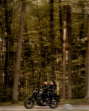 A motorcycle ride through a moody forest creates a dramatic engagement photo.