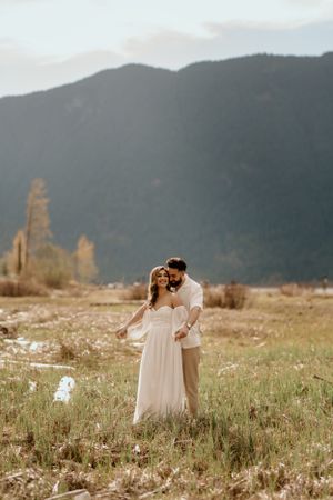 Couple embracing in mountain meadow during golden hour with mountains in background.