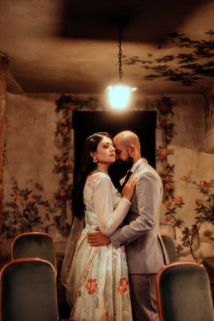 Romantic couple embraces in warmly lit vintage interior with floral wallpaper.
