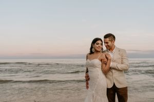 Couple in wedding attire sharing intimate moment on beach at sunset.