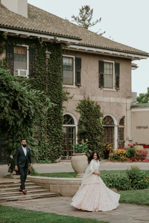 A couple poses outside an ivy-covered mansion with elegant landscaping.