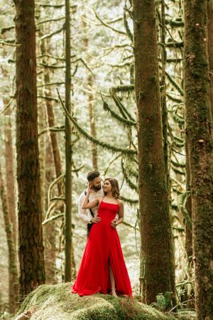 Figure in flowing red dress poses dramatically among tall forest trees.