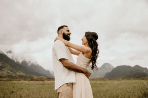 A couple embraces in a romantic pose with dramatic mountain peaks in the background.