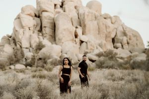 A couple in black attire poses against towering desert rock formations.